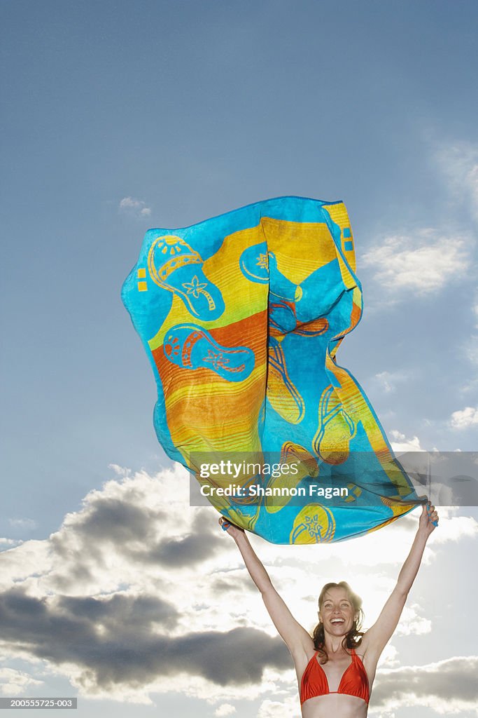 Woman waving beach towel against sky