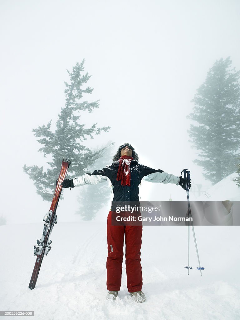 Young woman looking up holding skies and ski poles, full length