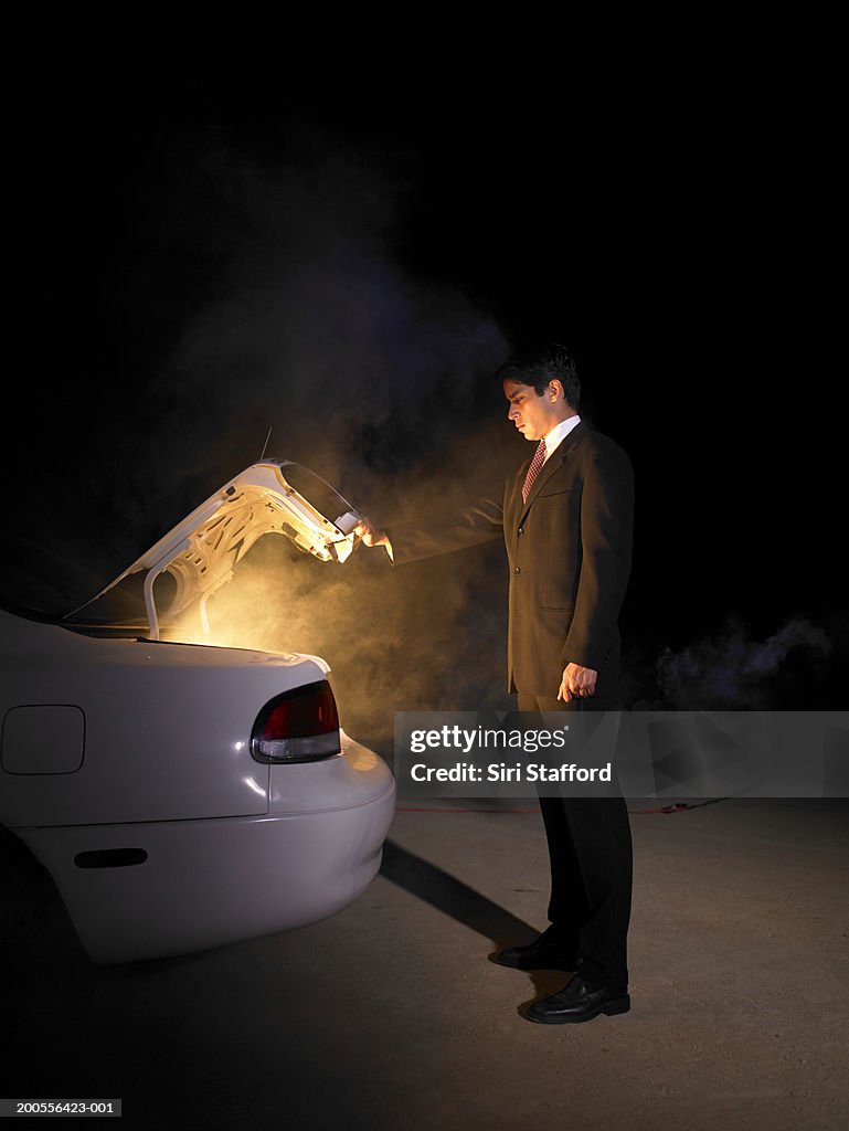 Businessman looking into glowing trunk of car