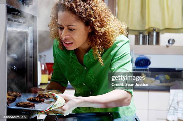 woman taking burnt cookies from oven - burnt stockfoto's en -beelden