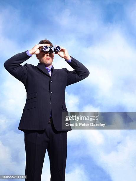 young businessman looking through binoculars, standing against sky - spy glass businessman stock pictures, royalty-free photos & images