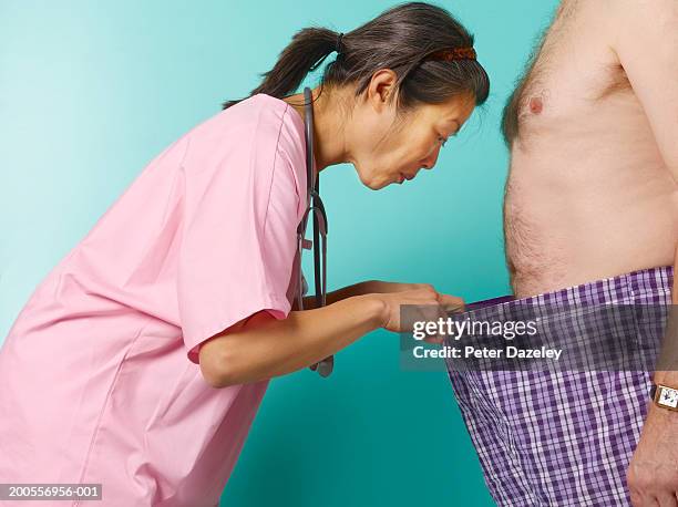 female doctor looking down into barechested man's pants, profile - pants down woman fotografías e imágenes de stock