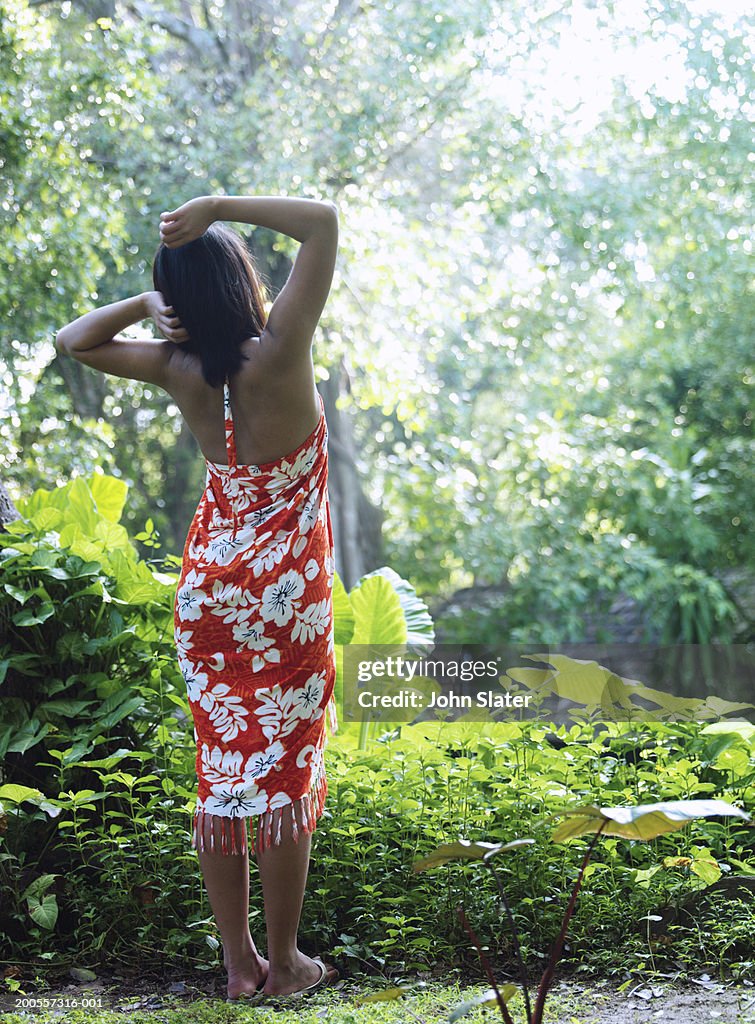 Young woman wearing sarong standing in garden, rear view