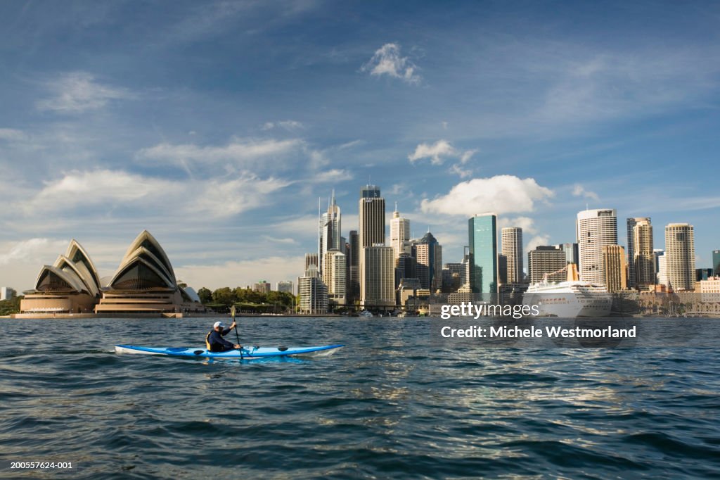 Australia, Sydney, person canoeing against city skyline, side view
