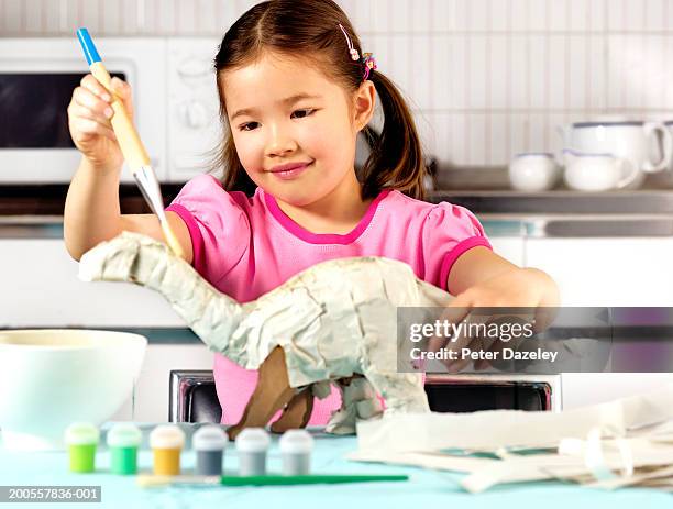 young girl (6-7) in kitchen, making paper dinosaur, smiling - papier mache bildbanksfoton och bilder