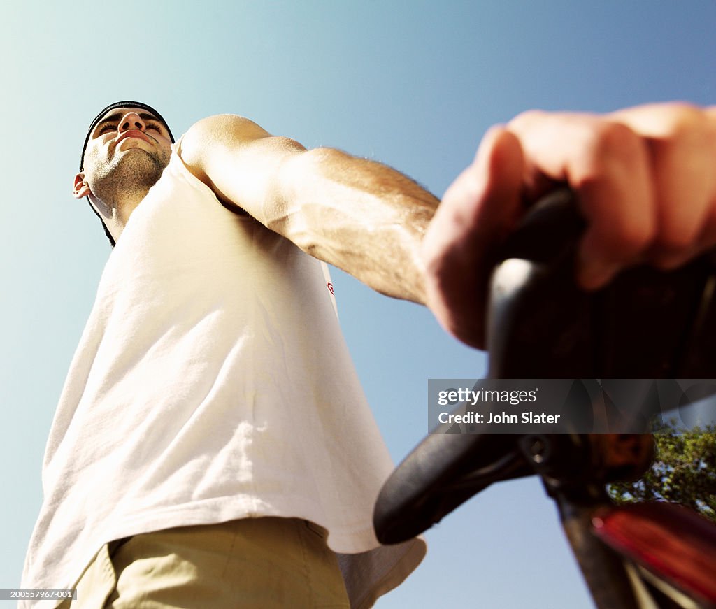 Young man leaning on bicycle outdoors, low angle view