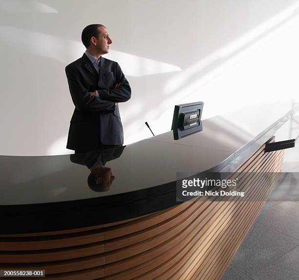 man standing with arms crossed at reception desk - pre reception stockfoto's en -beelden