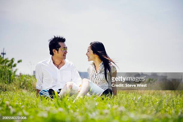 mid adult couple sitting on grass, smiling - mid adult couple stockfoto's en -beelden
