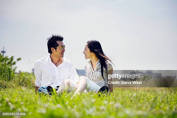 mid adult couple sitting on grass, smiling - mid adult couple stock pictures, royalty-free photos & images