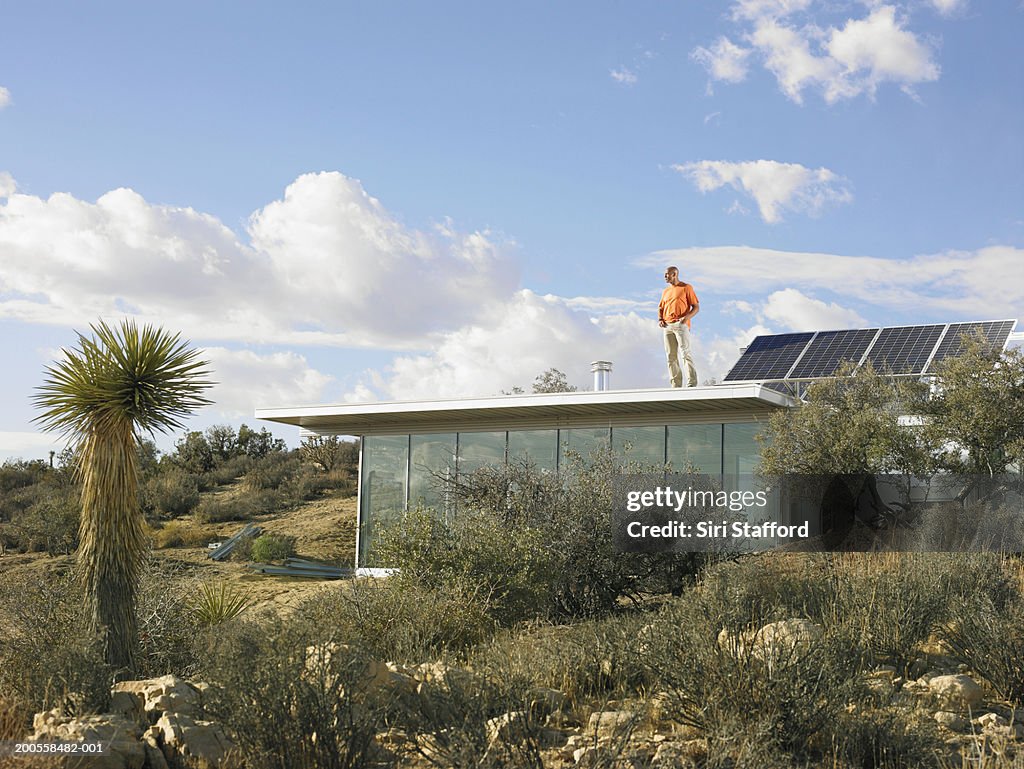 Man standing atop roof of prefabricated home with solar panels