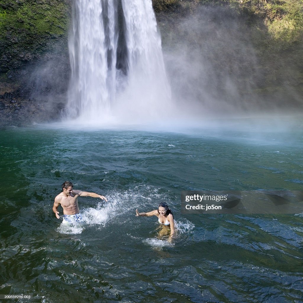 Young couple playing under Wailua Falls, elevated view