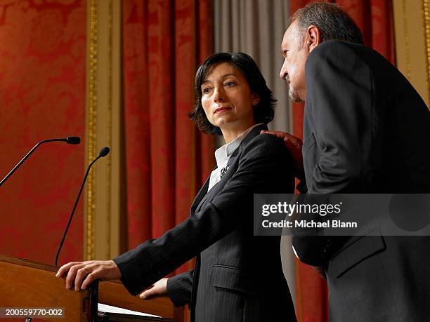 senior man whispering to politician woman standing at lectern - politician speaking stock pictures, royalty-free photos & images