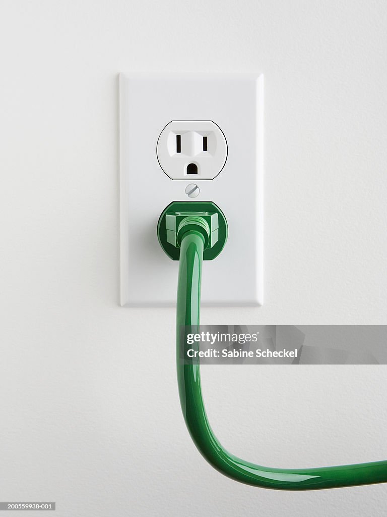 Plug socket with green power cable on wall, close-up