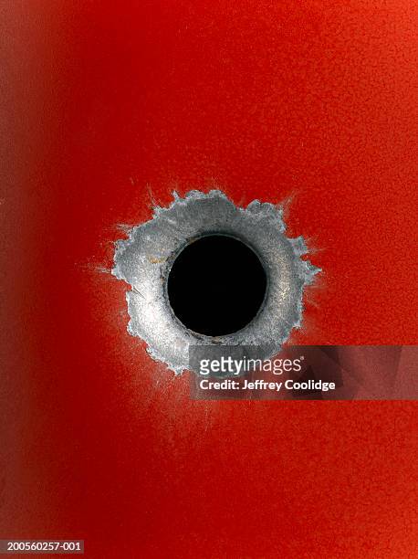 close-up of bullet hole in red metal surface - bullet holes stock-fotos und bilder