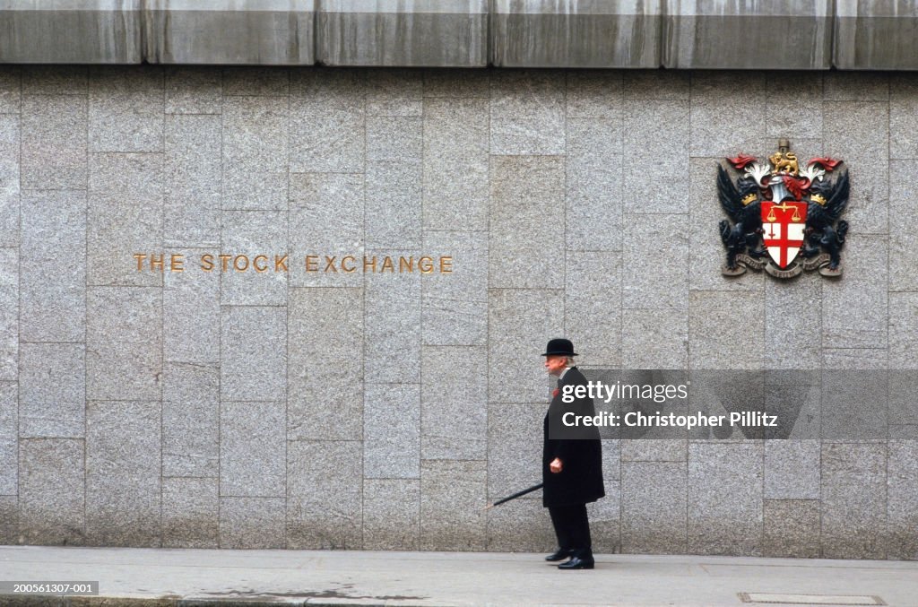 UK, London, senior man walking outside The Stock Exchange, side view