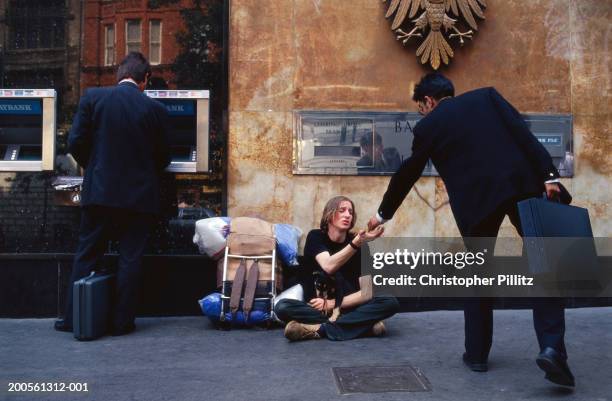 London Businessman giving money to beggar sitting beside ATM.