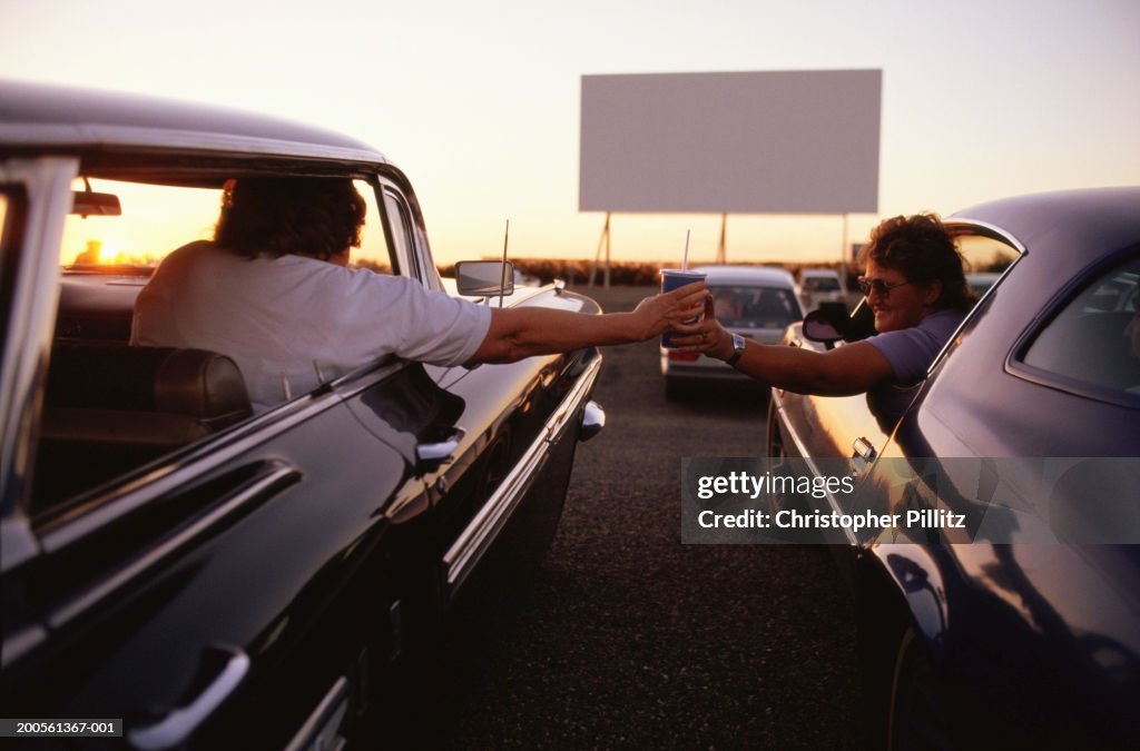 Men passing cup between cars in drive-in cinema, rear view