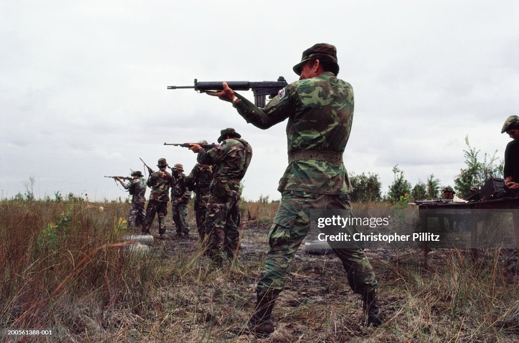 Soldiers pointing with guns in field, side view