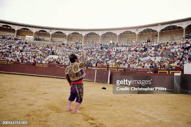 Spain, bullfighter in ring, waving at spectators, rear view.