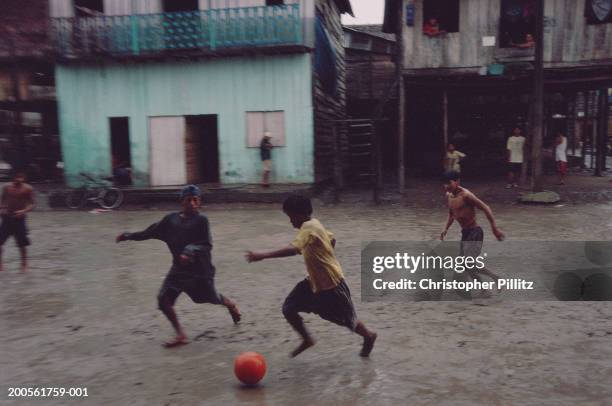 Peru, Iquitos, boys playing football in muddy street.