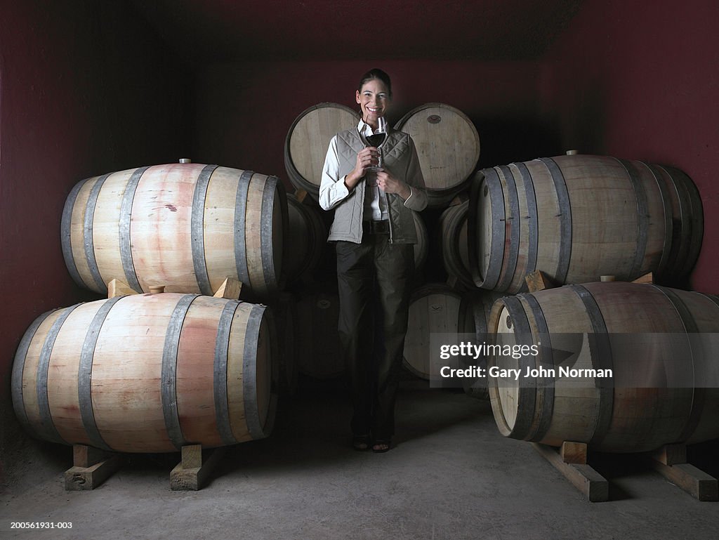 Woman standing by barrels in wine cellar, smiling, portrait