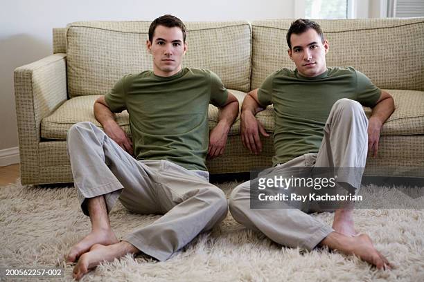 twin brothers sitting in living room, portrait - gémellité photos et images de collection