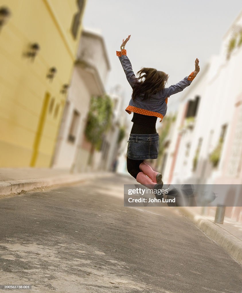 Woman jumping in street, rear view