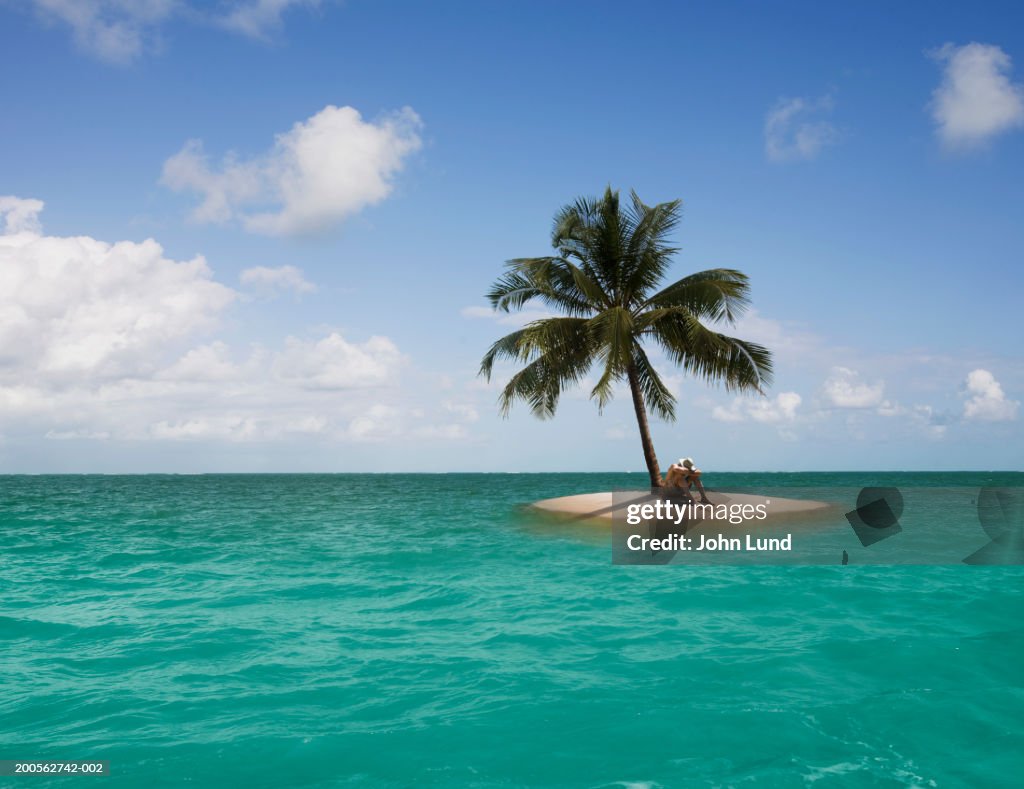 Man sitting on edge of small island with one palm tree