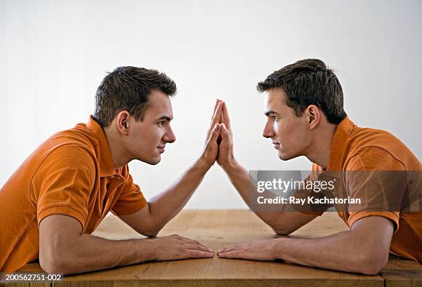 young male twins sitting at table face to face, touching palms,profile - gémeo idêntico imagens e fotografias de stock