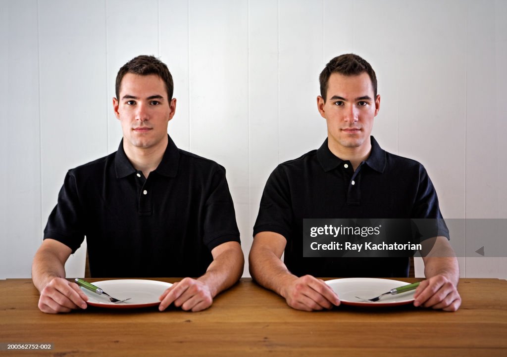 Young male twins sitting at table with empty plates, portrait