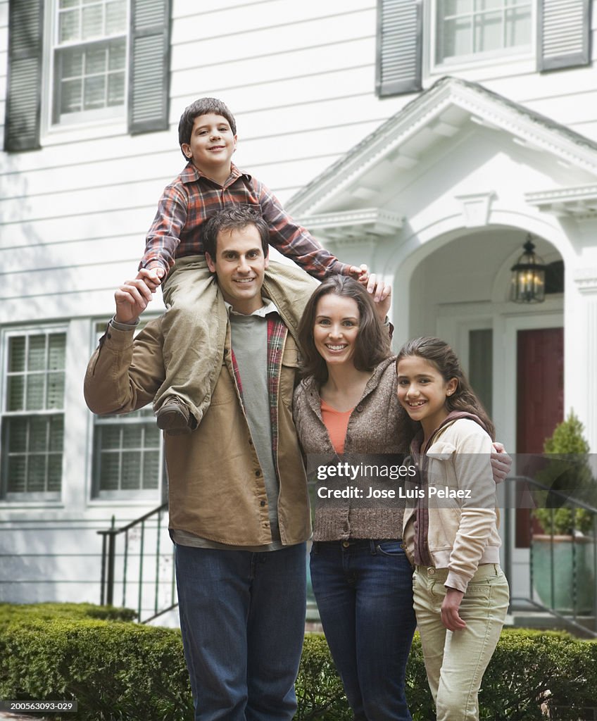Family including son (4-5), daughter (8-9) in front of house, smiling