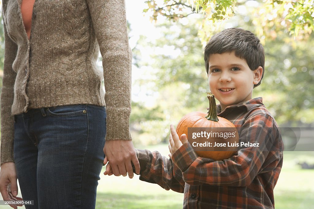 Mother and son (4-5), boy carrying pumpkin,smiling,trees in background