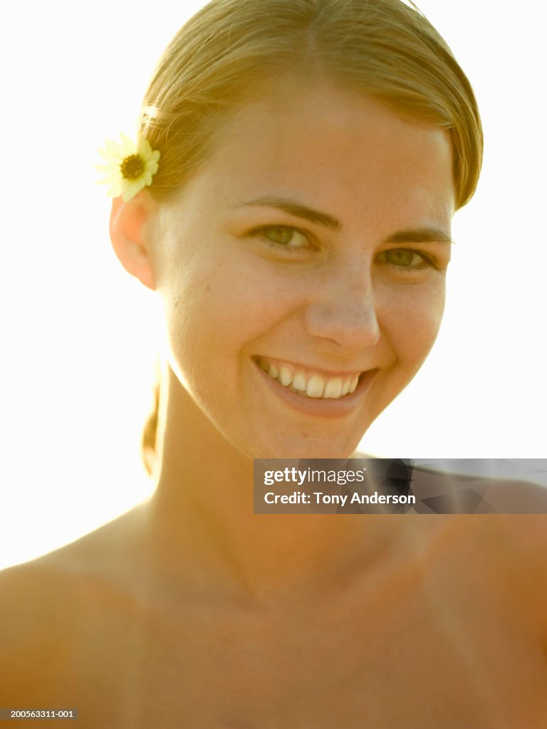 Young woman with flower in hair, smiling, portrait, close-up
