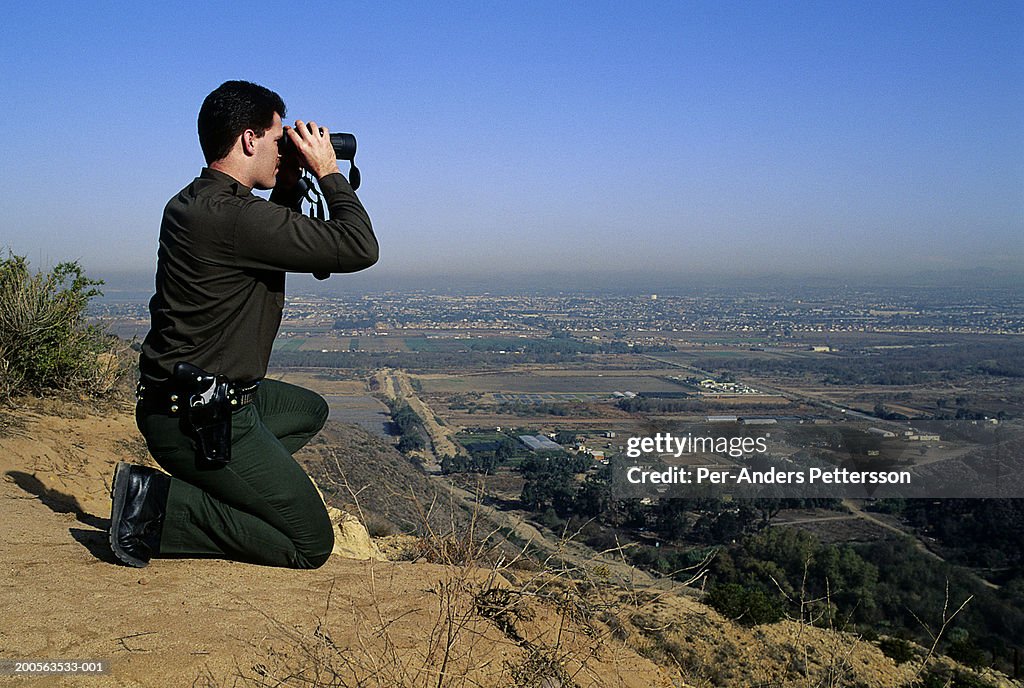 American officer of Border Patrol on hill observing Mexican border