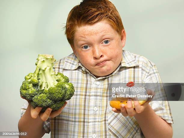 overweight boy (10-11) holding up head of broccoli and cake, portrait - grasso nutrienti foto e immagini stock