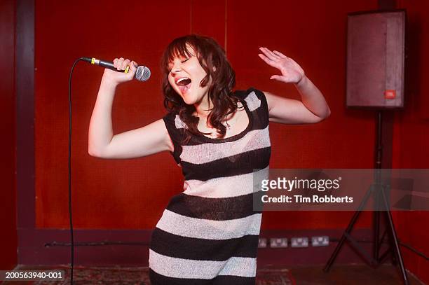young woman in striped dress singing into microphone on stage - karaoke stock pictures, royalty-free photos & images