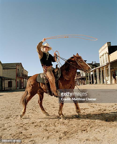 mature cowboy riding horse and lassoing - vaquero fotografías e imágenes de stock