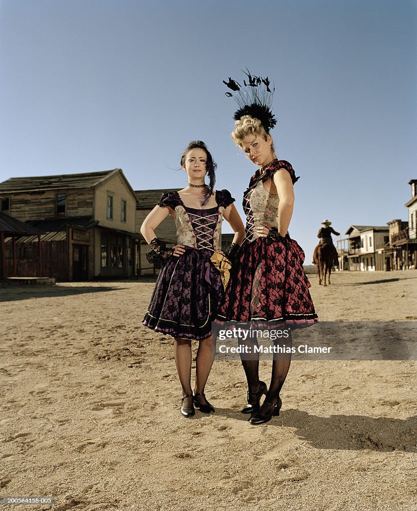 Showgirls standing with hand on hip, cowboy riding horse in background