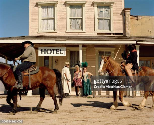 cowboy standing with showgirl with other cowboy riding horse - old west town stock pictures, royalty-free photos & images