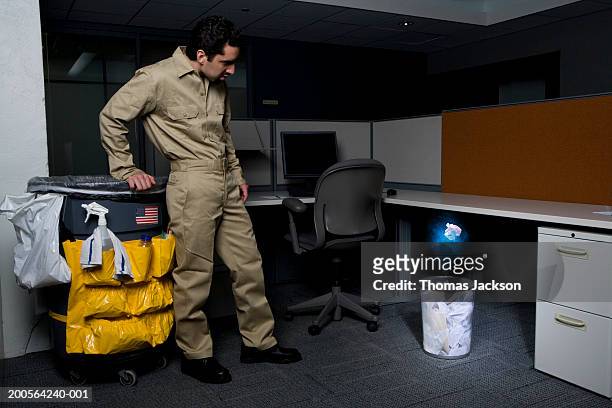 janitor in office, surprised by glowing paper rising from wastebasket - bidello foto e immagini stock