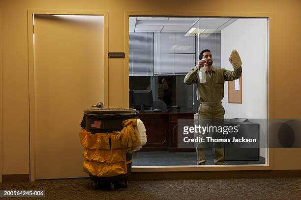 janitor in office late at night, cleaning window - bidello foto e immagini stock