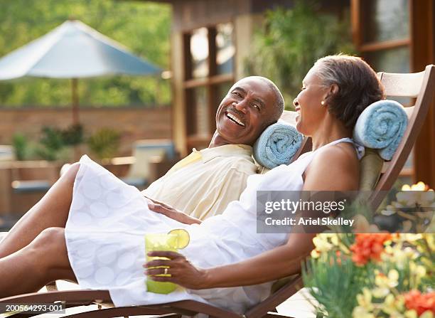 couple relaxing on sun lounger, smiling, side view - relaxing spa stock pictures, royalty-free photos & images