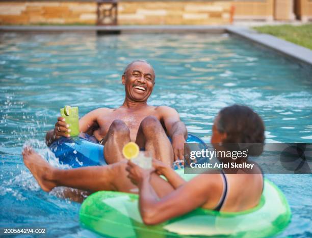 couple in rubber tube relaxing in pool, holding cocktail, laughing - old woman in swimsuit stock pictures, royalty-free photos & images