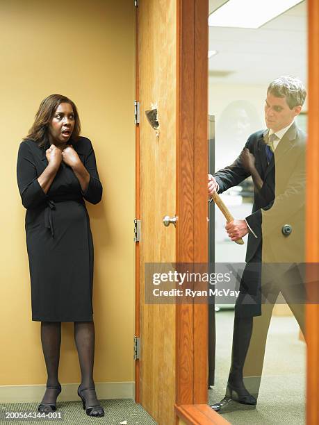 businesswoman hiding behind office door, man breaking door with axe - broken door stock-fotos und bilder