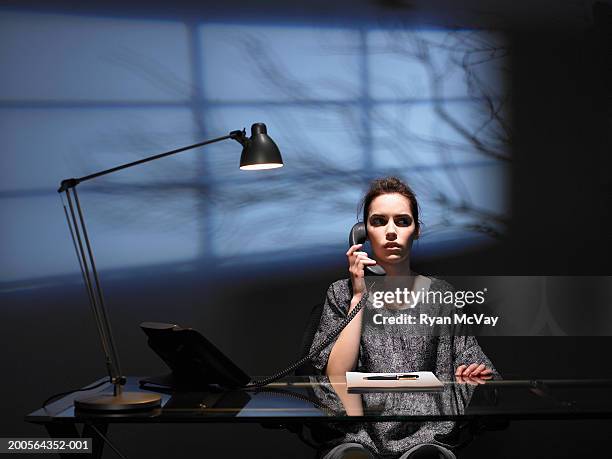 businesswoman at desk,using phone,shadow of tree behind window on wall - unheilschwanger stock-fotos und bilder