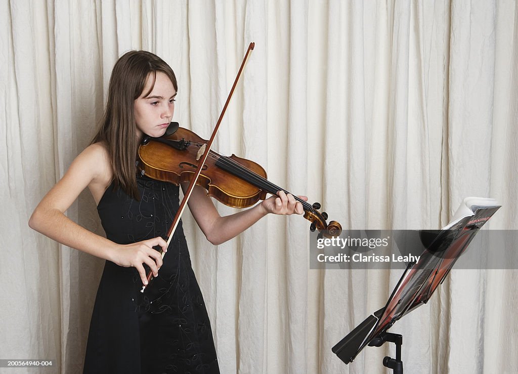 Girl (10-11 years) playing violin in front of curtain