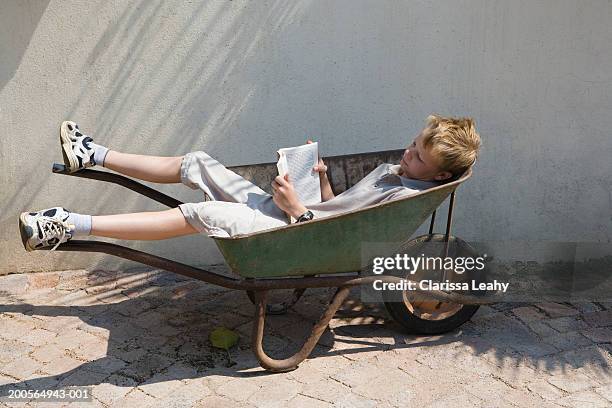 boy (12-13 years) reading book, lying in wheelbarrow, elevated view - 12 13 years stock pictures, royalty-free photos & images