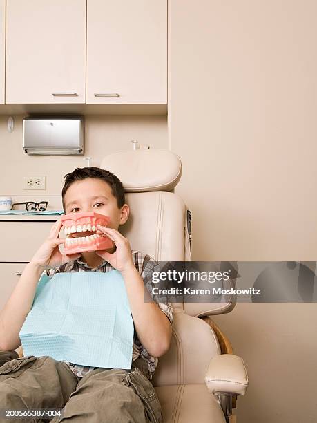 boy (6-7) in dentist's chair holding up model of teeth - dentista bambini foto e immagini stock