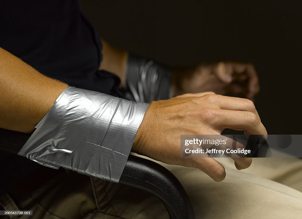 Man's wrists taped to arms of chair, close-up