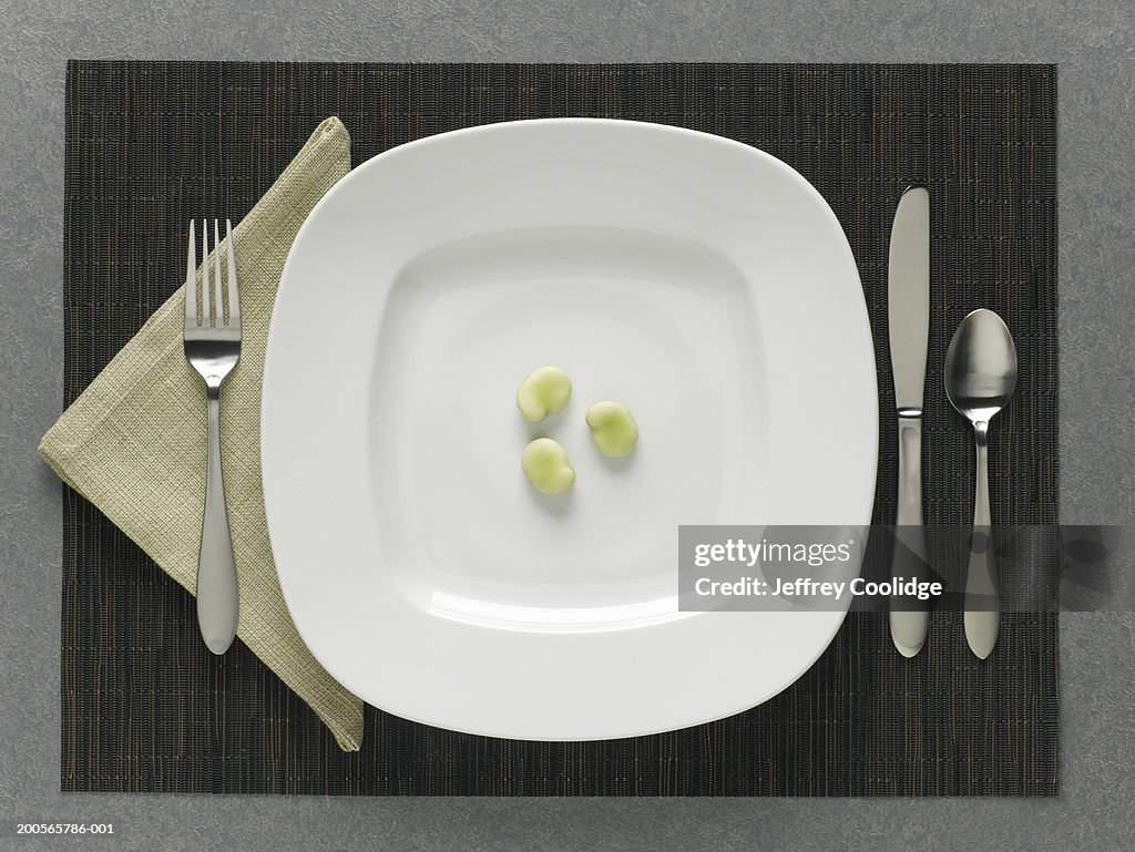 Three Fava beans on plate with table setting, elevated view